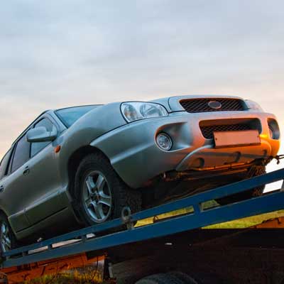 car being pulled onto the bed of a tow truck on a country road during sunset
