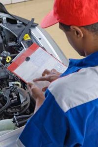 mechanic with clipboard looking of car engine bay