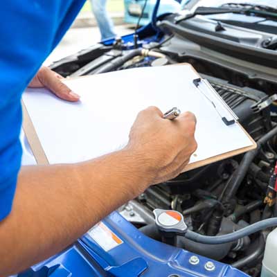 mechanic with clipboard leaning over engine bay